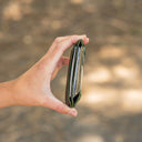 A hand holding an open slim black wallet or card holder against a blurred outdoor background.